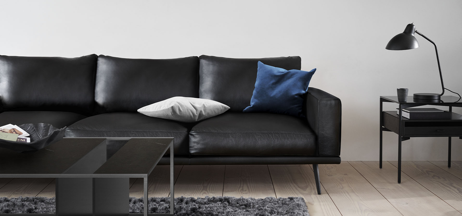 BoConceptin musta Carlton-nahkasohva, jonka päällä on kaksi eriväristä koristetyynyä